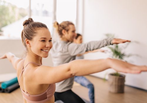 Smiling sporty woman doing warrior pose in yoga class. Happy young female practicing yoga at gym class.